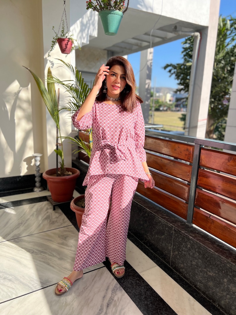 May include: A pink and white patterned palazzo pant set with a tie waist top. The set is made of a lightweight fabric and is perfect for warm weather.