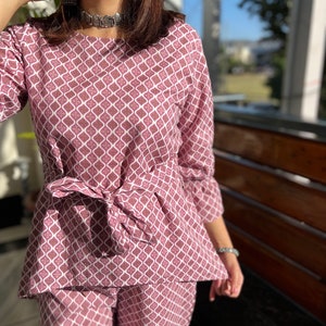 May include: A pink and white patterned two-piece outfit with a tie at the waist.