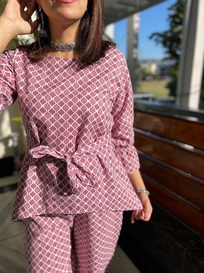 May include: A pink and white patterned two-piece outfit with a tie at the waist.