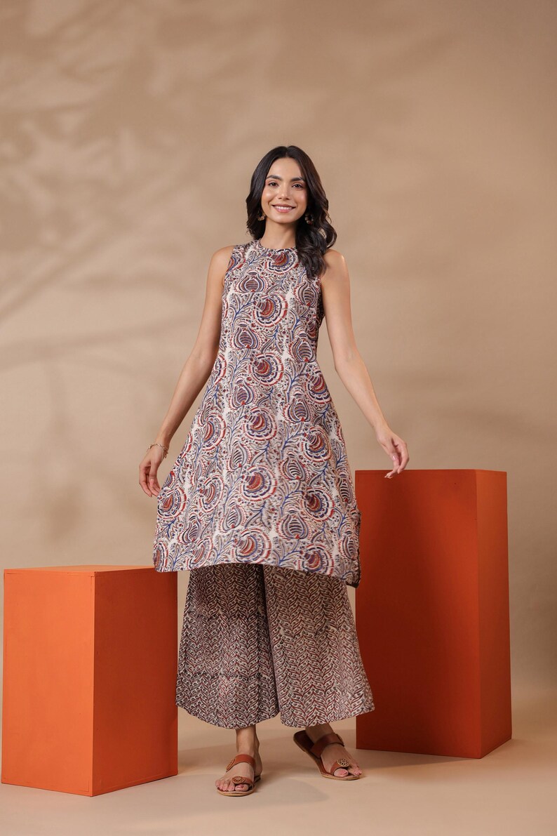 May include: A sleeveless tunic and wide-leg pants set. The tunic features a white base with a paisley pattern in red and blue. The pants have a complementary brown and white pattern. The outfit is suitable for casual wear.