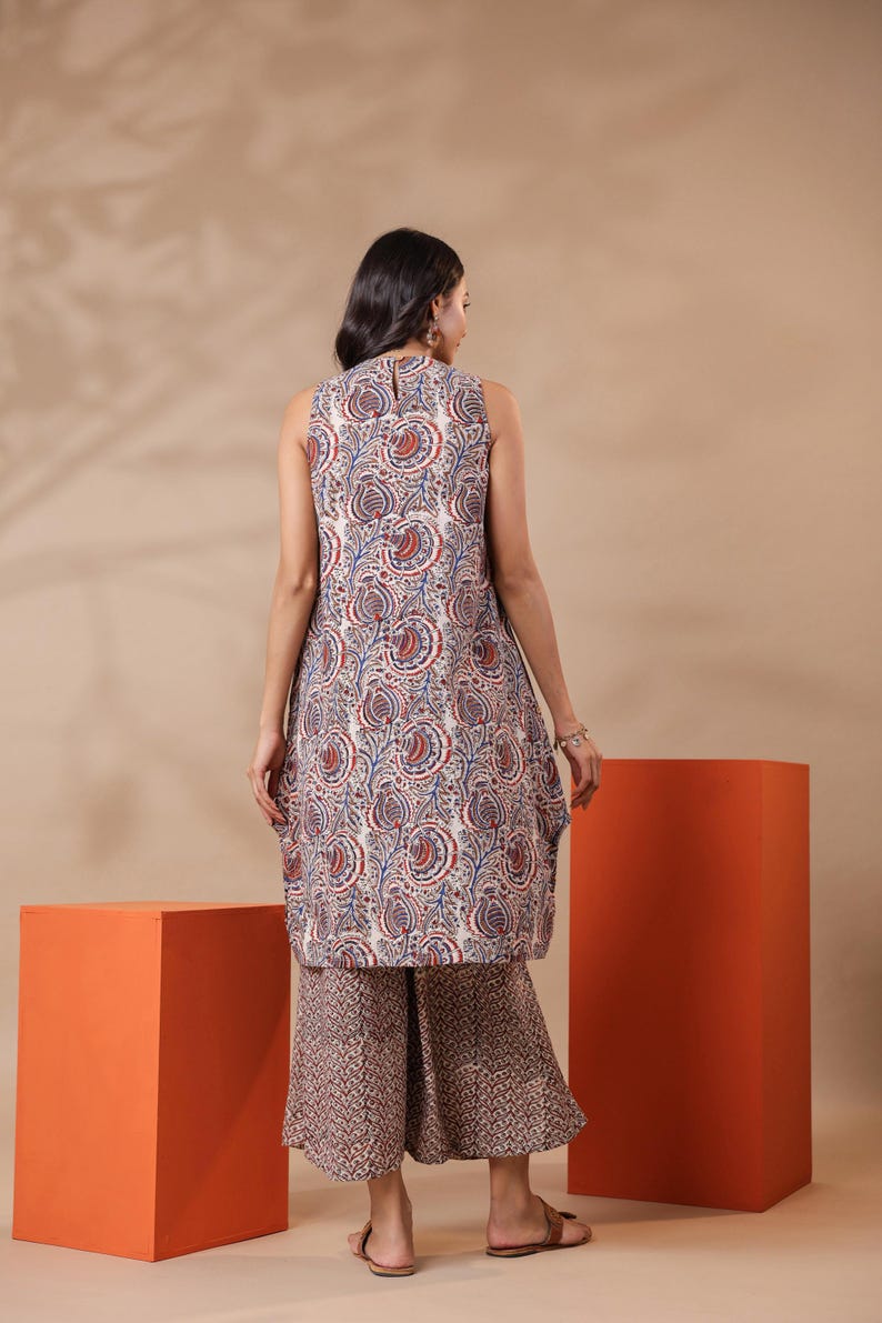 May include: A sleeveless tunic and wide-leg pants set. The tunic features a white base with a paisley pattern in red and blue. The pants have a complementary brown and white geometric print. The outfit is suitable for casual wear.