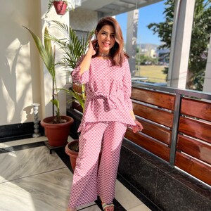 May include: A pink and white patterned pajama set with a tie at the waist. The top has 3/4 sleeves and the pants are wide-legged.