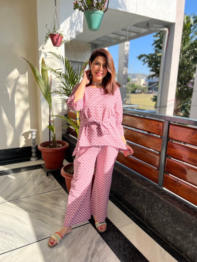 May include: A pink and white patterned pajama set with a tie at the waist. The top has 3/4 sleeves and the pants are wide-legged.