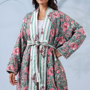 May include: A long, floral-print robe in teal and pink. The robe features a striped collar and belt, with a matching floral pattern. The sleeves are long, and the robe is tied at the waist. The floral pattern includes pink flowers and green leaves.