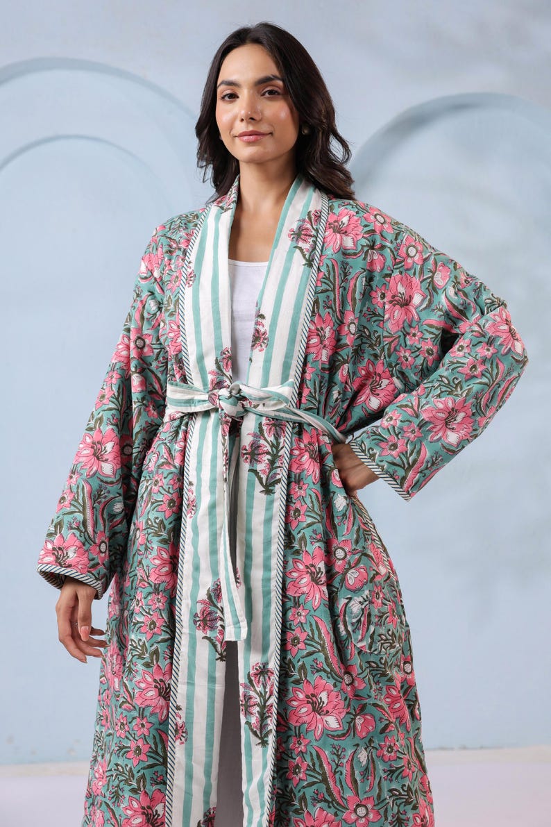 May include: A long, floral-print robe in teal and pink. The robe features a striped collar and belt, with a matching floral pattern. The sleeves are long, and the robe is tied at the waist. The floral pattern includes pink flowers and green leaves.