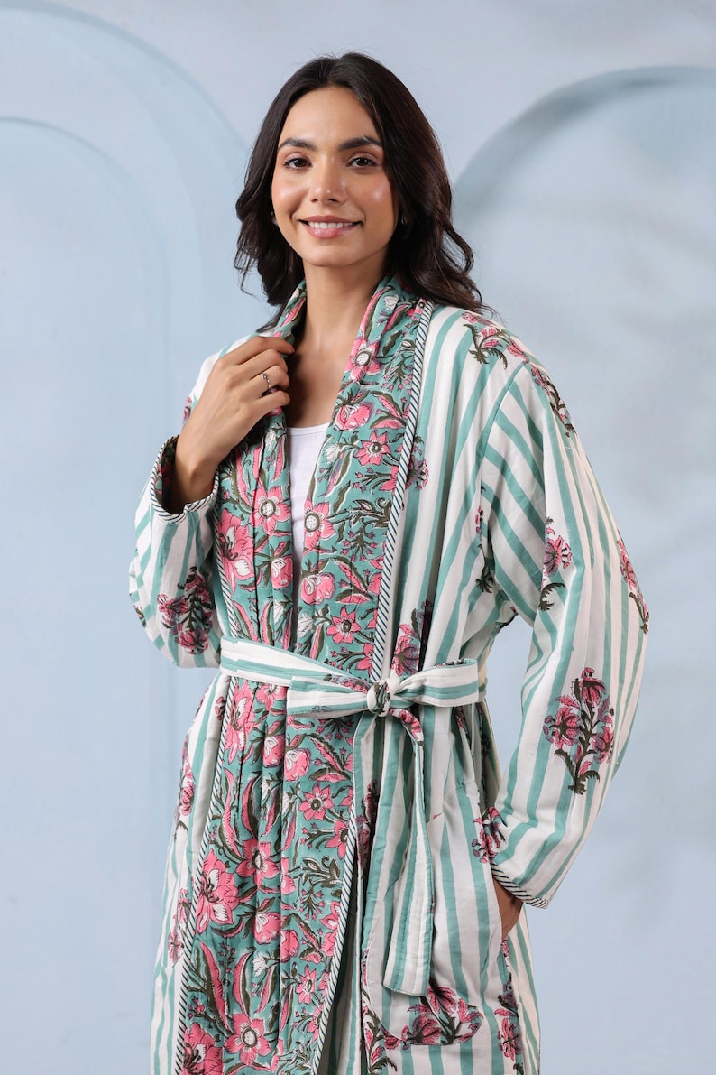 May include: A floral print robe with a striped pattern in shades of white, teal, and pink. The robe has a matching belt and a floral design on the collar and cuffs. The robe is made of a soft, lightweight fabric.