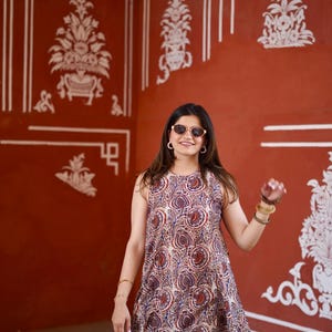 May include: A sleeveless dress and matching pants with a paisley pattern in shades of red, blue, and beige. The outfit is worn in a room with red walls and white decorative accents. The person is wearing sunglasses and bracelets.
