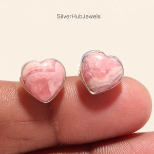 Könnte beinhalten: Ein Paar silberne herzförmige Ohrringe mit rosafarbenen Rhodochrosit-Edelsteinen. Die Ohrringe sind in Sterlingsilber gefasst und haben eine polierte Oberfläche.