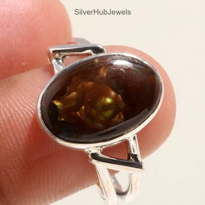 Puede incluir: Un anillo de plata con una piedra preciosa de ágata marrón y verde. El anillo tiene un diseño simple y moderno con una banda cruzada.