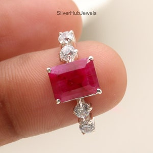 May include: A silver ring featuring a large, rectangular, deep red gemstone as the focal point. The ring is accented with smaller, clear gemstones on the band. The text "SilverHubJewels" is visible in the background.