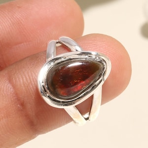 May include: A silver ring with a teardrop-shaped red gemstone set in a silver bezel. The ring has a simple, elegant design.