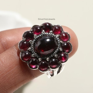 May include: A silver ring with a large red garnet gemstone surrounded by smaller red garnet stones.
