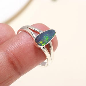 May include: A silver ring featuring a green and black oval opal gemstone. The ring has a double band design.