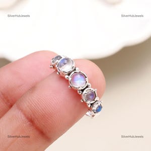 Könnte beinhalten: Ein silberner Ring mit fünf runden Mondstein-Edelsteinen, die in einem zarten Silberband gefasst sind. Der Ring befindet sich an einem Finger.