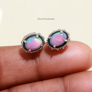 May include: A pair of silver earrings with iridescent opal stones set in a delicate, ornate design. The stones have a pink, green, and blue hue.