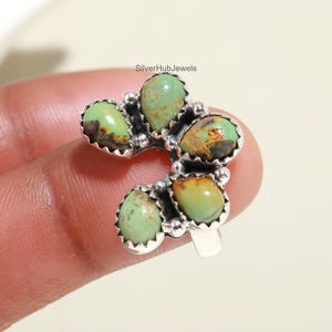 May include: A silver ring featuring six turquoise stones set in a flower design. The stones display a combination of green and brown hues.