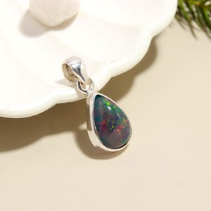 May include: A teardrop-shaped silver pendant with a black opal gemstone. The opal has a rainbow of colors, including red, green, and blue.