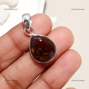 Peut inclure: Un pendentif en argent avec une pierre d'agate brune en forme de larme. Le pendentif est tenu dans une main.