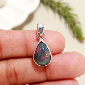 May include: A teardrop-shaped black opal pendant set in sterling silver. The opal displays a rainbow of colors, including red, green, and blue.