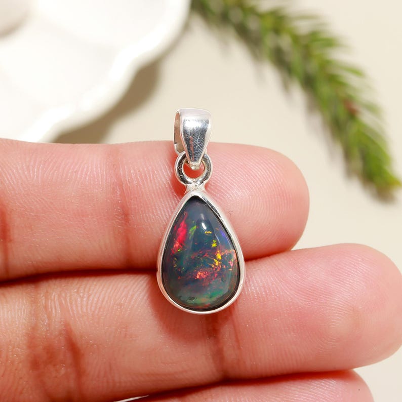 May include: A teardrop-shaped black opal pendant set in sterling silver. The opal displays a rainbow of colors, including red, green, and blue.