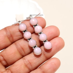 Puede incluir: Un par de pendientes colgantes de plata con piedras de ópalo rosa. Cada pendiente tiene cinco piedras, y las piedras están engastadas en un engaste de plata.