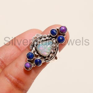 May include: A silver ring featuring an opal center stone with a leaf design, surrounded by blue and purple gemstones. The ring has a detailed, ornate setting. The text "Silver wels" is visible.