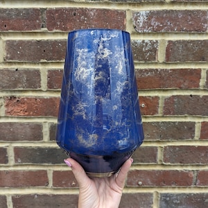 May include: A blue glass vase with a textured, marbled design. The vase has a wide base and a narrow neck.