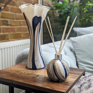 May include: A white and blue glass vase with a ruffled top and a round, white and blue glass diffuser bottle with wooden sticks.