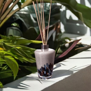 May include: A diffuser bottle with a grey and brown speckled design and a set of wooden sticks. The bottle is sitting on a white surface.