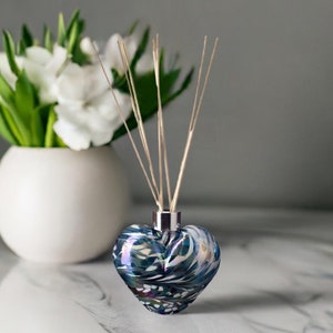May include: A heart-shaped glass diffuser bottle with a silver cap and blue and white swirling pattern. The bottle is filled with diffuser sticks.