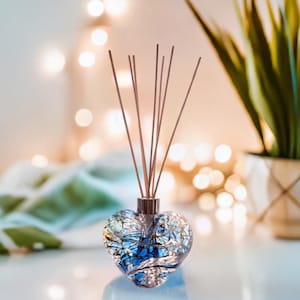 May include: A heart-shaped glass diffuser with blue and silver swirls, filled with a clear liquid and topped with wooden diffuser sticks.