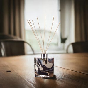 May include: A black and white marbled glass diffuser bottle with wooden sticks. The bottle is sitting on a wooden table.