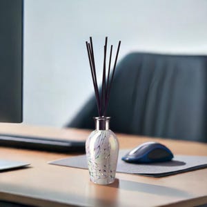 Op de afbeelding: Een witte, iriserende glazen diffuserfles met zwarte rietjes. De fles heeft een zilveren dop en staat op een houten oppervlak.