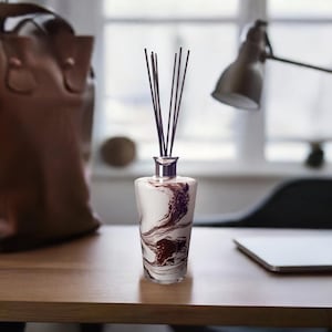 May include: A white and brown marble diffuser bottle with black reeds. The bottle has a silver cap and a swirling pattern.