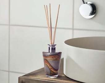 May include: A diffuser bottle with a grey, orange and brown marbled design and wooden sticks. The bottle is sitting on a wooden surface.