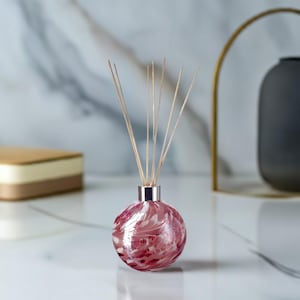 May include: A pink and white glass diffuser bottle with a silver lid and wooden sticks. The bottle has a swirl pattern.