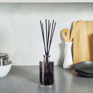 May include: A black glass diffuser bottle with a marble-like pattern and black reeds. The bottle is sitting on a white countertop.