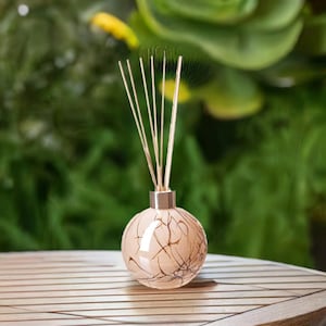 May include: A round glass diffuser bottle with a beige and brown marbled design. The bottle has a gold lid and is filled with brown reeds.