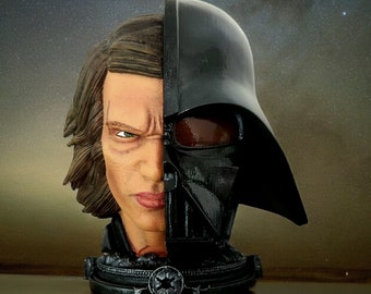 May include: A split-face bust sculpture depicting Anakin Skywalker and Darth Vader. The sculpture is half Anakin with brown hair and a stern expression, and half Darth Vader in a black helmet. The base has a Star Wars emblem.