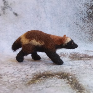 May include: A brown and black needle felted wolverine figurine with a white stripe on its back. The figurine is walking with its head turned to the side.