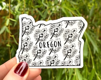 May include: A white sticker with a black outline of the state of Oregon. The sticker has a floral pattern and the word "OREGON" in the center.
