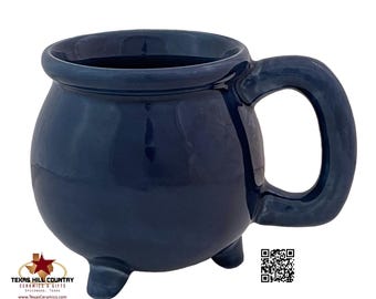 May include: A dark blue ceramic cauldron mug with a handle and three feet. The mug is glazed and has a smooth finish.