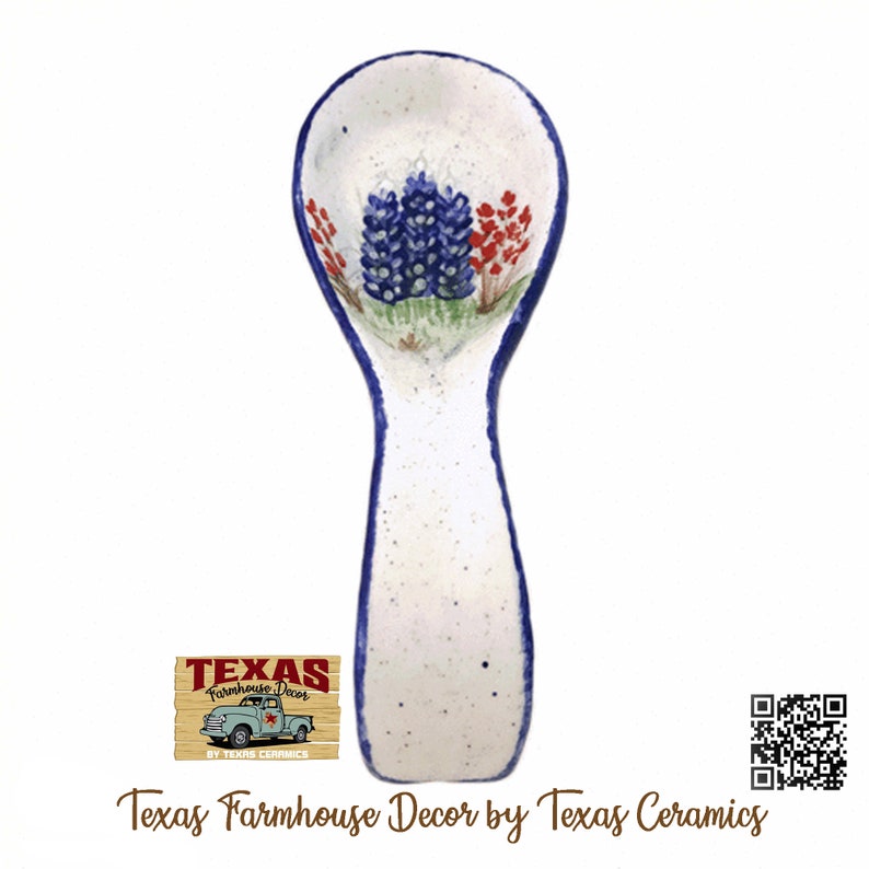 May include: White ceramic spoon rest with a blue and red floral design. The spoon rest has a blue border and is speckled with small black dots. The text "Texas Farmhouse Decor by Texas Ceramics" is at the bottom.