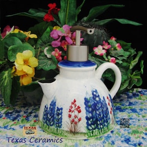 May include: White ceramic teapot with a blue rim and a stainless steel pump. The teapot is decorated with bluebonnet flowers and red accents. The text "Texas Ceramics" is visible at the bottom.