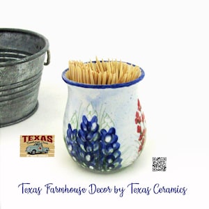 May include: A ceramic toothpick holder with a blue rim and floral design, filled with wooden toothpicks. The holder features bluebonnet and red flower illustrations. A galvanized metal bucket is in the background. The text "Texas Farmhouse Decor by Texas Ceramics" is at the bottom.