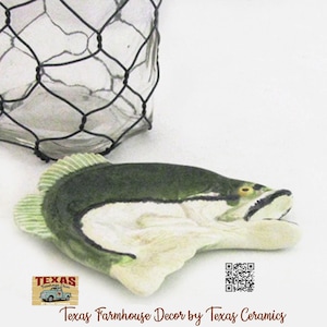 May include: A white ceramic mug with a black handle and the text "But First, Coffee" in a black, handwritten-style font. The mug is on a white surface.