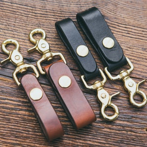 May include: Four leather keychains with brass swivel clips and brass snap closures. Two keychains are brown leather and two are black leather.
