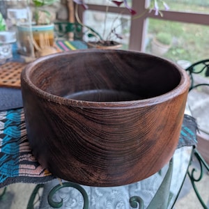 Könnte beinhalten: Eine dunkelbraune Holzschale mit zylindrischer Form. Die Schale hat eine glatte, polierte Oberfläche und sichtbare Holzmaserung. Der Innenraum ist leer und die Schale steht auf einer Glasoberfläche.