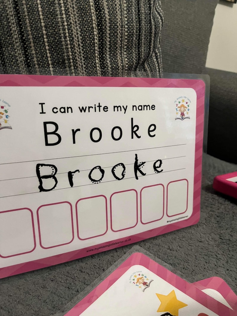 Pode incluir: Cart&atilde;o de aprendizagem rosa e branco com o texto "Eu posso escrever meu nome Brooke" e um espa&ccedil;o para escrever o nome. O nome Brooke est&aacute; escrito em marcador preto abaixo do texto. H&aacute; seis espa&ccedil;os em branco abaixo do nome para praticar a escrita.