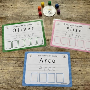 Pode incluir: Tr&ecirc;s cart&otilde;es laminados coloridos com uma linha pontilhada e espa&ccedil;os em branco para praticar a escrita de nomes. Os cart&otilde;es s&atilde;o verde, rosa e azul e apresentam os nomes "Oliver", "Elise" e "Arco".